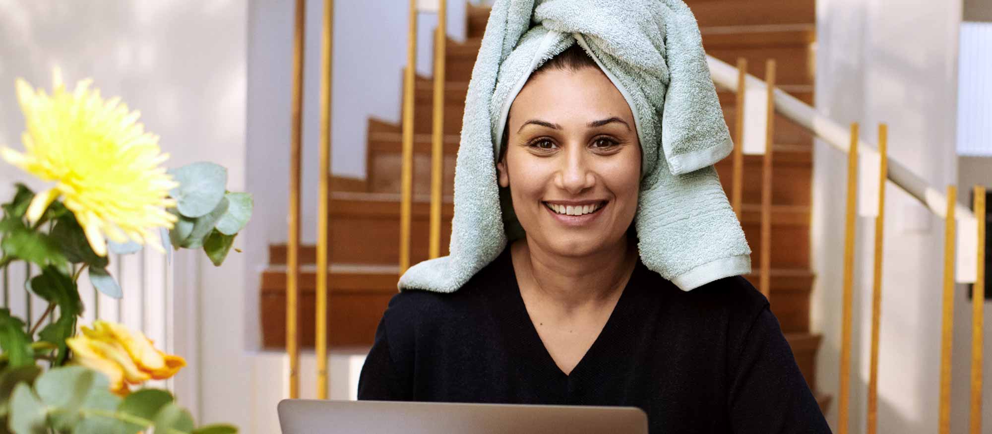 Glad kvinna med en blå handuk om håret sitter hemma framför en dator